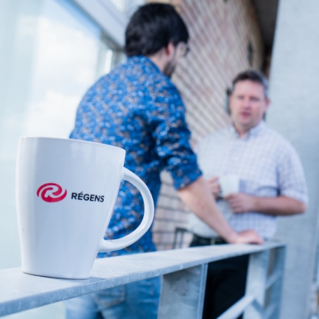 2 men standing on a balcony communicating with a mug in the foreground